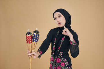 Beautiful Asian model wearing black kebaya dress with hijab, holding a bamboo torch over beige...