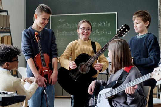 Group of cheerful teen boys and girls with musical instruments having break during rehearsal in classroom