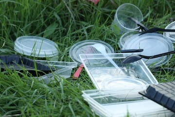 Used plastic tableware on grass outdoors, closeup. Environmental pollution concept