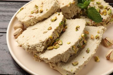 Pieces of tasty halva with pistachios and mint on table, closeup