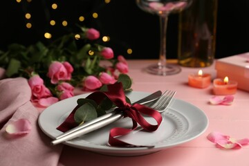 Place setting with roses and candles on pink wooden table, closeup. Romantic dinner