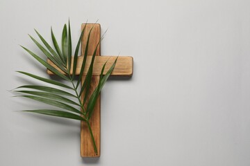 Wooden cross and palm leaf on light grey background, top view with space for text. Easter attributes