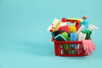 Different cleaning products in plastic basket on light blue background, space for text