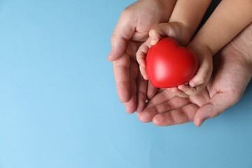 Obraz premium Father and his child holding red decorative heart on light blue background, top view. Space for text