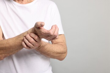 Arthritis symptoms. Man suffering from pain in wrist on gray background, closeup. Space for text