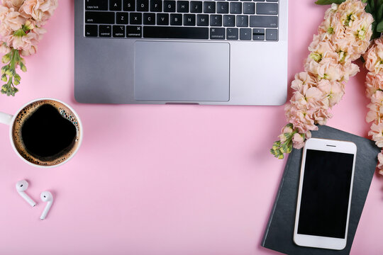 Cropped shot of feminine workspace with laptop, matthiola flowers and cup of black coffee. A bouquet for international women's day in the office. Pink background, copy space, flat lay, close up.