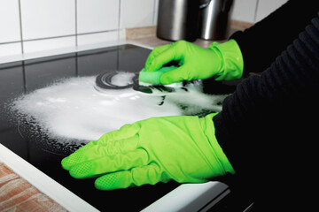 A man wearing cleaning gloves wipes the induction hob.