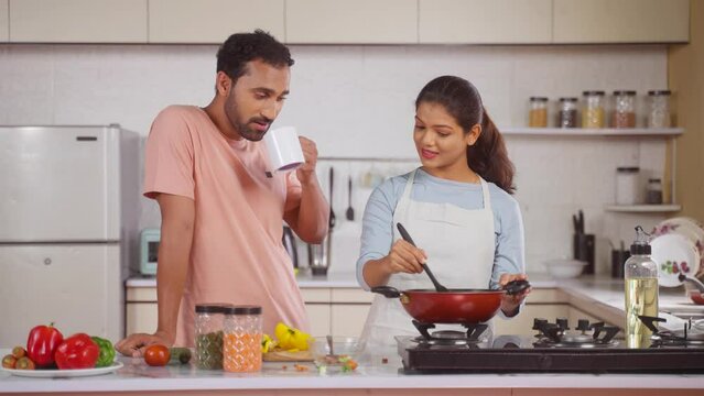 happy husband with coffee spending time with cooking wife at kitchen - concept of relationship bonding, morning routine and family affection.