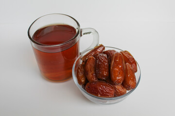 Deglet noor or deglet nour or date palm or dates, in a transparent bowl, with a glass of tea, isolated on white background