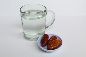 Three pieces of Deglet noor or deglet nour or date palm or dates, with a glass of water, isolated on white background