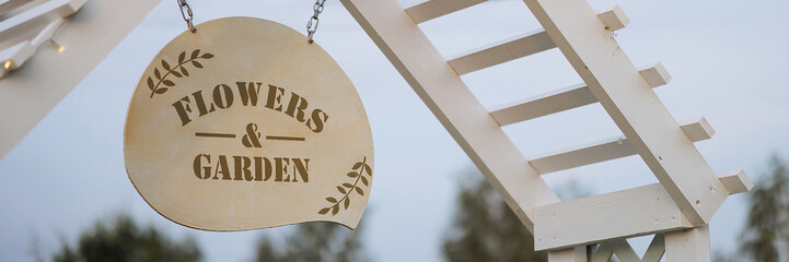 A round Flowers and Garden sign hangs from a white, wooden structure. Concept for garden...