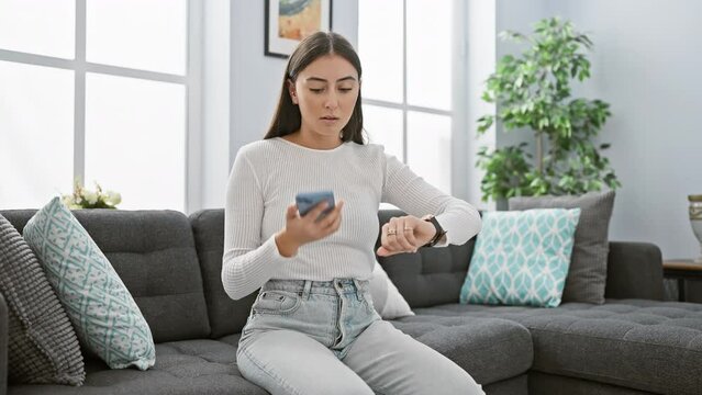 Hispanic woman checking time while talking on smartphone in a modern living room.