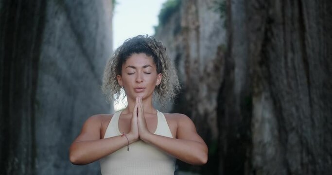 Portrait of a young Latin woman with curly hair who performs breathing and yoga practices against the backdrop of white rocks. She breathes deeply and smiles Yoga improves the balance of body and mind