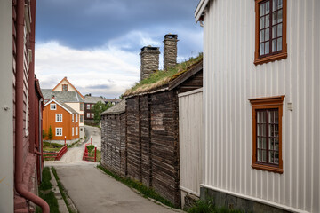Fototapeta na wymiar Nestled within the historic village of Roros, this street view captures the unique charm of timber walls and sod roofs, with a pop of color from traditional Norwegian houses