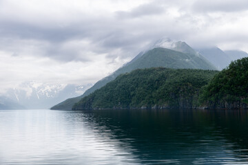 Misty clouds caress the mountaintops and blanket the lush greenery of Norway's fjord country, with...