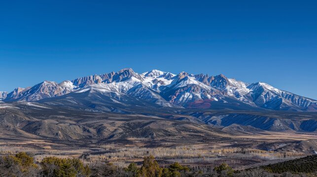 Panoramic view of a mountain range with snowy peaks under a clear blue sky.