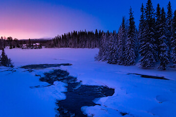 Swedish Winter Wonderland: Frozen River Glowing in Sunrise Amidst Forested Banks in Northern Europe