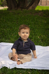 Bebé de un año sentado sobre una manta blanca en un parque iluminado con la luz del día