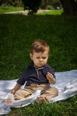 Bebé de un año sentado sobre una manta blanca en un parque iluminado con la luz del día