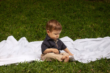 Bebé de un año sentado y jugando sobre una manta blanca en un parque iluminado con la luz del día