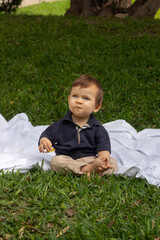Bebé de un año sentado sobre una manta blanca en un parque iluminado con la luz natural del día