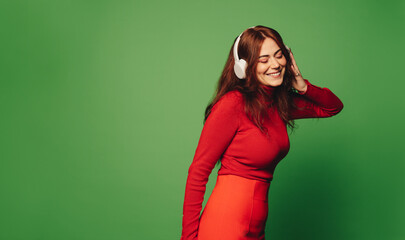 Obrazy na Szkle  Cheerful young woman enjoying music on headphones in modern studio