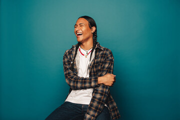 Joyful young man man with braided hair and cultural jewelry sitting and laughing in a studio