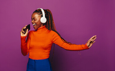 Happy girl singing and streaming music with headphones on purple background
