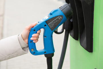 Young woman charging her electric car at the gas station, using a smartphone. Eco fuel concept. The concept of environmentally friendly transport. Recharging battery from charging station.