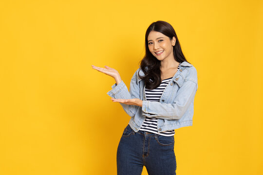 Happy Asian in jeans outfits presenting or showing open hand palm with copy space for new product isolated on yellow background