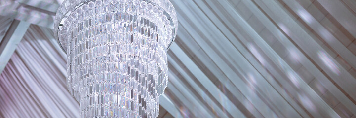 An elegant chandelier illuminates a banquet hall with a ceiling draped in transparent fabric....