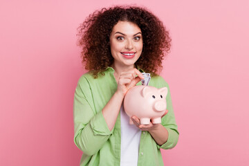 Fototapeta na wymiar Photo portrait of lovely young lady hold piggy insert banknote dressed stylish green garment isolated on pink color background