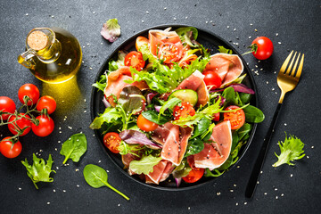 Healthy food. Fresh salad with jamon, green salad leaves and tomatoes. Top view with space for text.