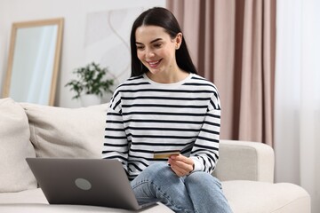Happy young woman with credit card and laptop shopping online at home