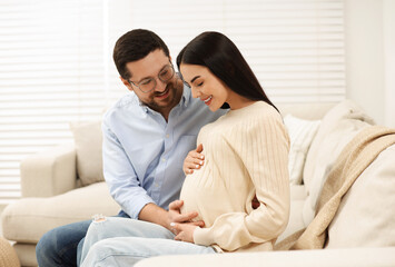 Happy pregnant woman spending time with her husband on sofa at home