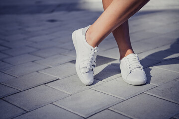 Close up cropped photo of girl legs foot wear new white trendy sneakers posing walking street outside