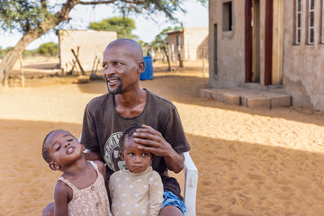 african village together with two of his daughters sited on a chair in the yard
