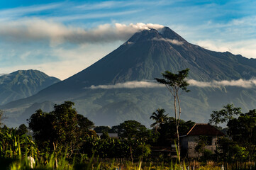 Beautiful Merapi volcano landscape view with tropical green trees foreground and cloudy blue sky...