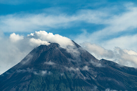 Merapi volcano crater close up view from south side showing solfatara gas eruption with cloudy blue sky background