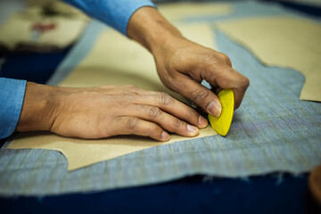 Young African American tailor drawing with chalk on material in his own atelier.