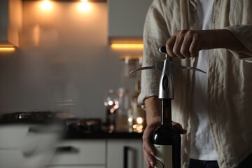 Man opening wine bottle with corkscrew in kitchen, closeup. Space for text