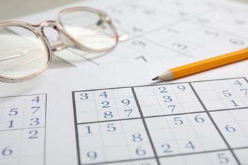 Sudoku, pencil and eyeglasses on table, closeup view