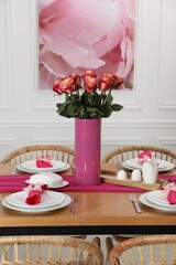 Color accent table setting. Plates, cutlery, pink napkins and vase with beautiful roses in dining room