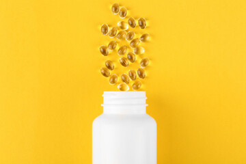 White medical bottle and vitamin capsules on yellow background, top view