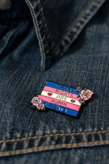 pin with the trans flag and with the message Trans rights are human rights, put on a denim shirt