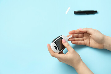Diabetes. Woman checking blood sugar level with glucometer on light blue background, top view....