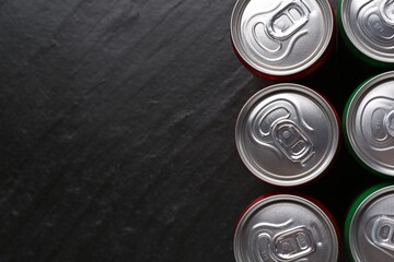 Energy drink in cans on black textured background, top view. Space for text