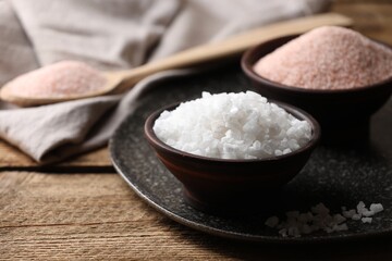 Different salt in bowls on wooden table, closeup. Space for text