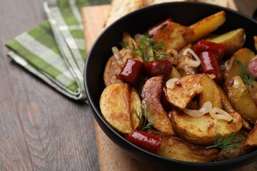 Delicious baked potato with thin dry smoked sausages, onion and dill in bowl on wooden table, closeup. Space for text