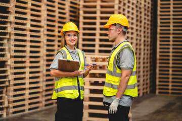 Man and woman workers with clipboard discussing working and checking stock inventory wood plank material for making wooden pallet products at warehouse industrial factory, woodwork production